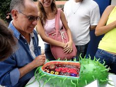 a group of people standing around a cake with green frosting and decorations on it