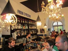 a group of people sitting at a bar in a room with chandeliers hanging from the ceiling