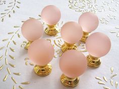 six pink glass knobs with gold accents on a white table cloth and doily