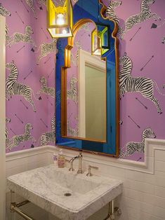 a bathroom with purple and blue wallpaper has a mirror on the wall above it