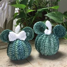 two crocheted mickey mouses sitting next to each other on a table with plants in the background