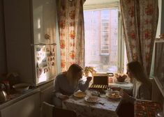 two women sitting at a table in front of a window eating cake and drinking coffee