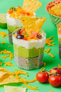 three cups filled with food and chips on top of a green table covered in confetti