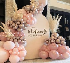 balloons are arranged in the shape of an arch with flowers and feathers on it, along with a sign that reads little wildflower is on her way