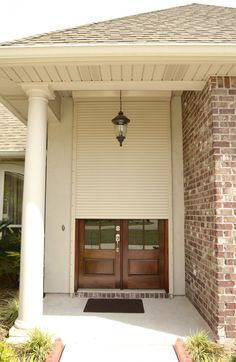 the front entrance to a home with two brown doors and brick pillars on either side