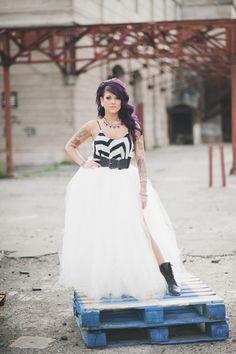 a woman with purple hair wearing a white dress and black boots standing on a pallet