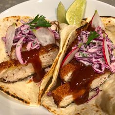 two fish tacos with cole slaw and lime wedges on a white plate