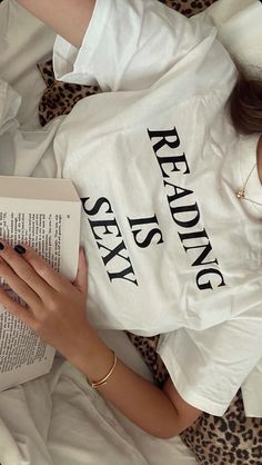 a woman reading a book while laying on top of a leopard print bed sheet with her hands resting on an open book