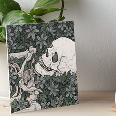 a drawing of a skull and flowers on a table next to a potted plant