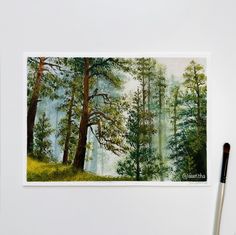 a painting of trees in the woods with watercolors on paper next to paintbrushes