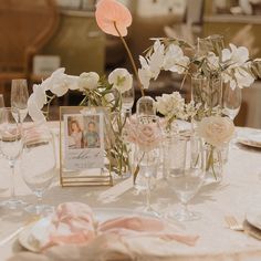 the table is set with white and pink flowers in vases, wine glasses, and cards