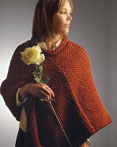 a woman is holding a rose and wearing a red knitted ponchy over her shoulders