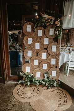 a table with place cards on it in front of a wall decorated with greenery