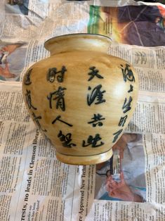 a vase with writing on it sitting on top of a newspaper page next to a pair of scissors