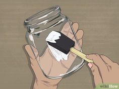 a hand holding a toothbrush in a glass jar filled with something black and white