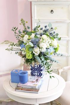 a blue and white vase filled with flowers sitting on top of a table next to a magazine