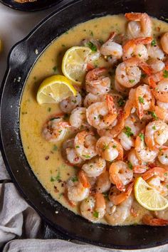 a skillet filled with shrimp and grits next to lemon wedges on a table