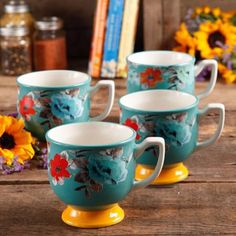 four tea cups sitting on top of a wooden table next to sunflowers and books