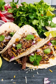 three shredded beef tacos with cilantro and lime