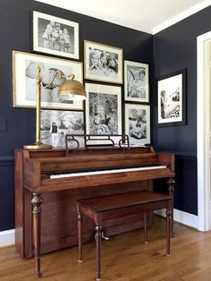 an old piano is in front of several framed pictures on the wall, along with a lamp