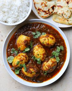 some food is in a white bowl on a table next to rice and pita bread