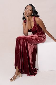 a woman sitting on top of a white block wearing a red dress and heels with her hand under her chin