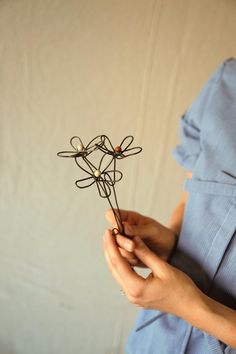 a woman in a blue dress is holding a small wire flower with her hands on it