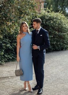 a man and woman standing next to each other in front of some bushes wearing formal attire