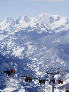 skiers and snowboarders at the top of a ski lift with mountains in the background