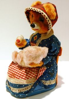 a teddy bear dressed in blue and red sitting on top of a basket with a doll