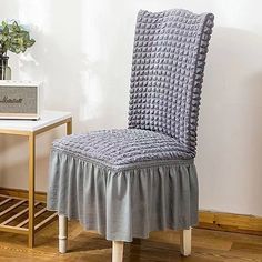 a gray chair with a ruffled seat cover on it next to a small table