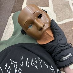 a person wearing a brown mask laying on the ground next to a black jacket and hat