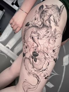 a woman's thigh with a dragon and flowers tattoo on it