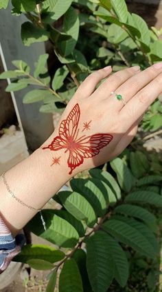 a woman's hand with a red butterfly tattoo on her left wrist and green leaves in the background