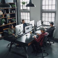 four people sitting at desks in an office setting with computers and laptops on them