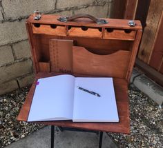 an open notebook sitting on top of a wooden box next to a pen and book