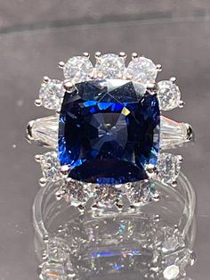 a blue and white diamond ring sitting on top of a glass table with diamonds around it