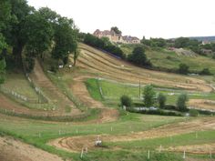 an aerial view of a dirt track with trees and houses on the hill in the background