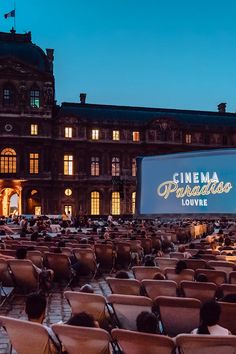 an outdoor movie is set up in front of a large building with many chairs around it