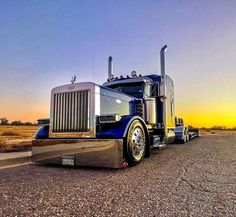 a semi truck is parked on the side of the road in front of an orange and blue sky