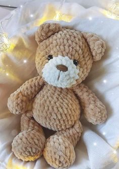 a brown teddy bear sitting on top of a white cloth covered pillow with lights in the background