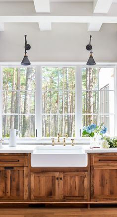 a kitchen with wooden cabinets and white counter tops, two large windows above the sink