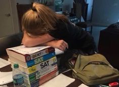 a person leaning their head on some books while sitting at a table with other items