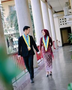 a man and woman walking down a hallway holding hands with medals on their necks