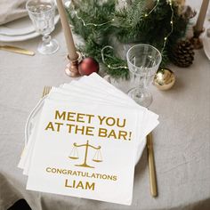 a table topped with white napkins covered in gold lettering next to candles and christmas decorations