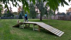 a person on a bike riding over a wooden ramp in the middle of a yard