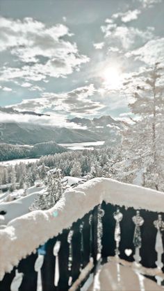 snow covered trees and mountains in the distance with sun shining through cloudy skies above them