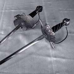 two metal swords are laying on a white sheet and one has a flower design on it