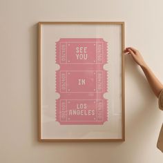 a woman holding up a pink poster with the words see you in los angeles