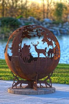 a metal globe with animals on it in the middle of a park next to a body of water